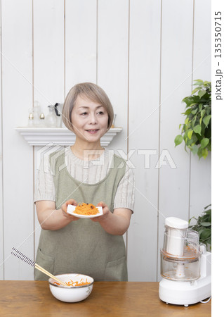 キッチンでフードプロセッサーを使い料理をするシニア女性 135350715