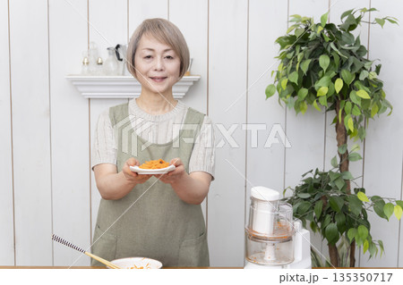 キッチンでフードプロセッサーを使い料理をするシニア女性 135350717