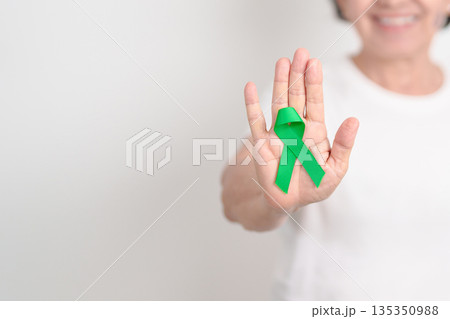 Elderly with Green Ribbon for concept of March world Bipolar disorder day, Cerebral Palsy Awareness month, kidney disease Cancer and Traumatic Brain Injury, TBI. Healthcare and world cancer day 135350988