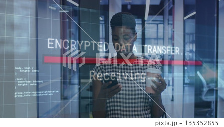 Holding smartphone and coffee cup, employee standing in office hallway with encrypted data overlay 135352855