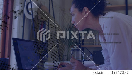 Leaning woman wearing white blouse analyzing code on laptop in office, with mug and French press 135352887