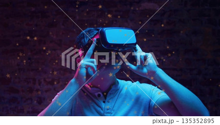 Man wearing light polo shirt adjusting virtual reality headset in studio, with star overlays Man wearing light polo shirt adjusting virtual reality headset in studio, with star overlays 135352895