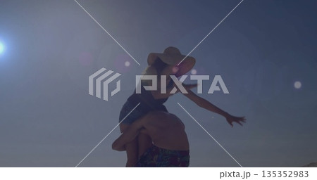 Shirtless man carrying woman on seaside beach, with straw sun hat, one piece swimsuit, swim trunks Shirtless man carrying woman on seaside beach, with straw sun hat, one piece swimsuit, swim trunks 135352983