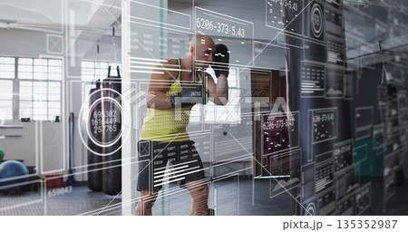 Performing shadow boxing drills male athlete in neon top and gloves in gym, with digital overlay 135352987
