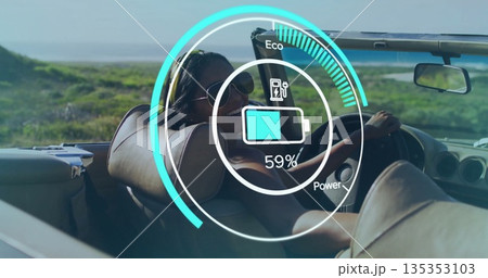 Driving Indian woman steering convertible along coastal highway, showing digital battery gauge 135353103