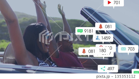 Driving couple in convertible raising arms through hills, with sunglasses, notification icons 135353112