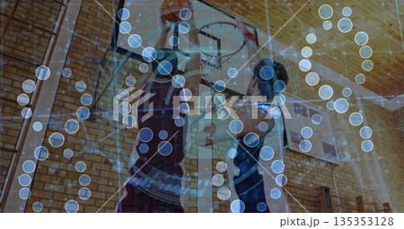 Leaping athletes performing dunk and block in gym, with basketball and hoop network overlay Leaping athletes performing dunk and block in gym, with basketball and hoop network overlay 135353128