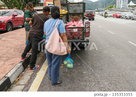 People buying fruits from a truck by the side of the road in a busy market area during the day 135353355