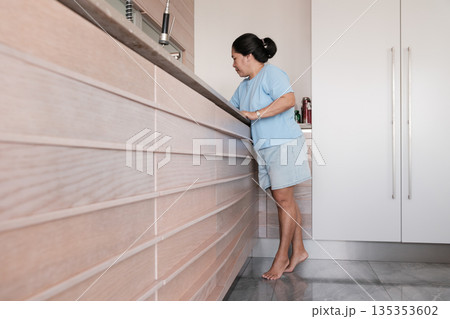 Woman stands in kitchen, preparing food while wearing casual clothes and barefoot in bright and modern home Woman stands in kitchen, preparing food while wearing casual clothes and barefoot in bright and modern home 135353602