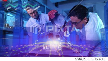 Researchers in goggles pouring from metal container into chamber in lab with digital finance graphs Researchers in goggles pouring from metal container into chamber in lab with digital finance graphs 135353716