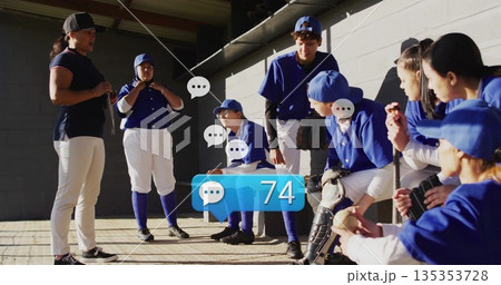 Coach holding bat and gesturing with team in blue jerseys in dugout, with speech icons, gloves 135353728