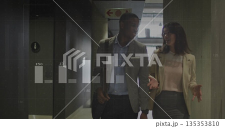 Walking colleagues in business attire carrying shoulder bag in office corridor with data overlays 135353810