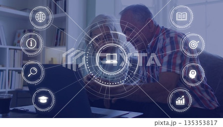 Studying senior couple exploring online network concepts at desk, with laptop smartphone icons 135353817