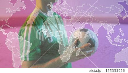 Holding soccer ball, male soccer player wearing green jersey standing in studio with world map Holding soccer ball, male soccer player wearing green jersey standing in studio with world map 135353926