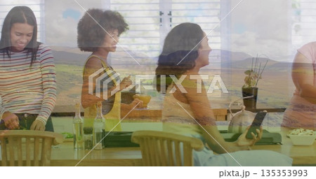 Preparing friends chopping vegetables and stirring mixture at kitchen island with mountain overlay 135353993