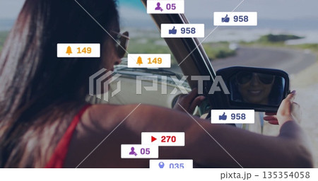 Adjusting mirror Indian woman with sunglasses driving on coastal road with media icons, copy space Adjusting mirror Indian woman with sunglasses driving on coastal road with media icons, copy space 135354058