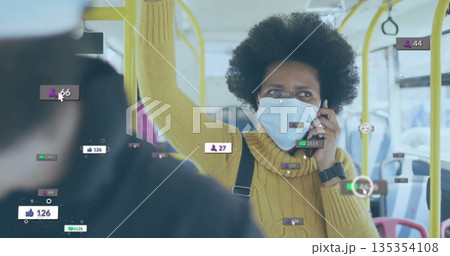 Talking commuter in yellow sweater wearing mask holding handrail on city bus, with smartphone 135354108