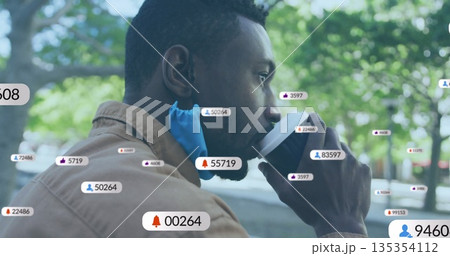 Sipping coffee from cup, man with blue face mask at park bench with floating social icons 135354112