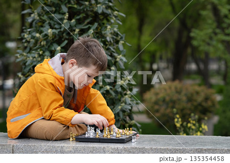 Boy playing chess outdoor. Learning strategic game. Education. Boy playing chess outdoor. Learning strategic game. Education. 135354458