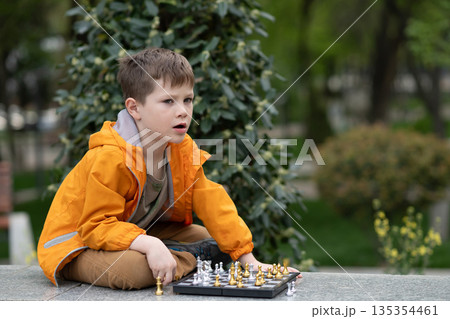 Boy playing chess outdoor. Learning strategic game. Education. Boy playing chess outdoor. Learning strategic game. Education. 135354461