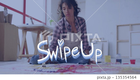 Painting female artist wearing apron applying vibrant paint onto canvas on studio floor, with jars Painting female artist wearing apron applying vibrant paint onto canvas on studio floor, with jars 135354564