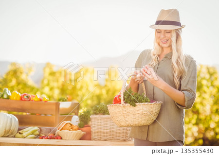 Female shopper wearing green shirt inspecting tomato and holding basket at farm stall, copy space Female shopper wearing green shirt inspecting tomato and holding basket at farm stall, copy space 135355430