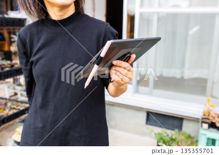 自宅の庭でタブレットを持っている、黒いシャツを着た女性の素材 135355701