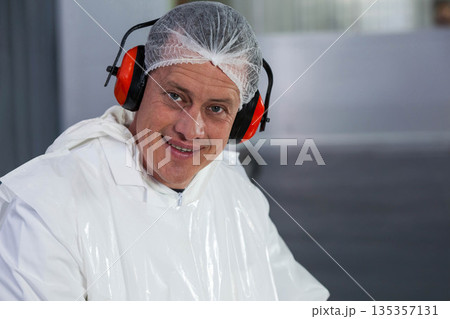 Male technician standing in production hall in protective coverall hairnet and earmuffs, copy space 135357131