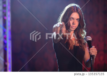 Female performer on club stage holding microphone and pointing at viewer under purple stage lights Female performer on club stage holding microphone and pointing at viewer under purple stage lights 135357135