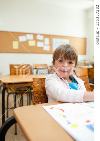 Female child drawing colorful artwork on paper at school desk beside bulletin board, copy space Female child drawing colorful artwork on paper at school desk beside bulletin board, copy space 135357282