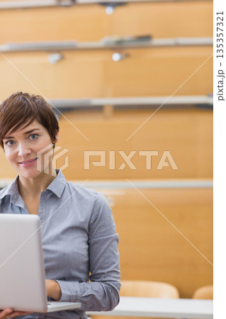 Woman working on laptop at desk in lecture hall with wooden benches and railings, copy space 135357321
