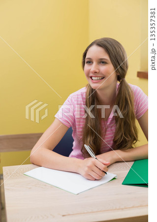 Teenage girl writing notes at wooden desk in study nook using silver pen and open notebook Teenage girl writing notes at wooden desk in study nook using silver pen and open notebook 135357381