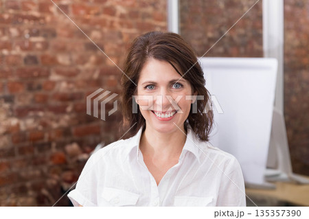 Adult woman smiling while standing in front of red brick wall with blank flip chart Adult woman smiling while standing in front of red brick wall with blank flip chart 135357390