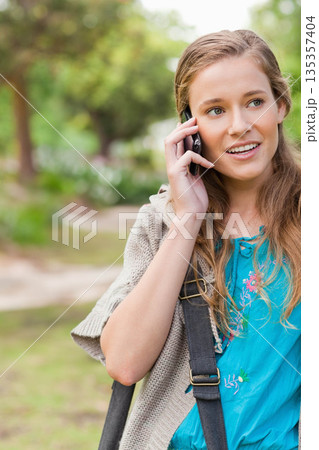 Woman talking on smartphone while walking on park walkway with backpack strap, copy space 135357404