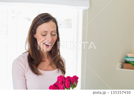 Woman holding pink roses bouquet by window beside shelf with green bowl and tan box Woman holding pink roses bouquet by window beside shelf with green bowl and tan box 135357430