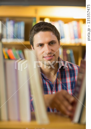 Man wearing plaid shirt browsing colorful books at wooden library bookshelf under warm lighting Man wearing plaid shirt browsing colorful books at wooden library bookshelf under warm lighting 135357475