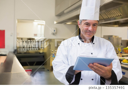 Holding tablet male chef in professional kitchen with steel counter, ventilation hood, copy space 135357491