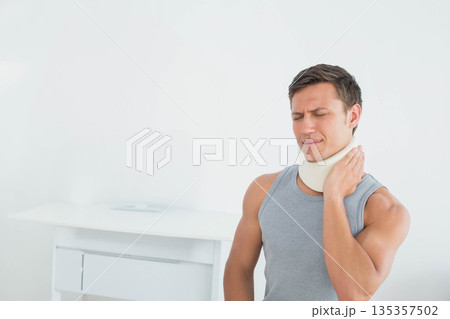 Male patient pressing cervical collar while standing in exam room with white cabinet, copy space 135357502