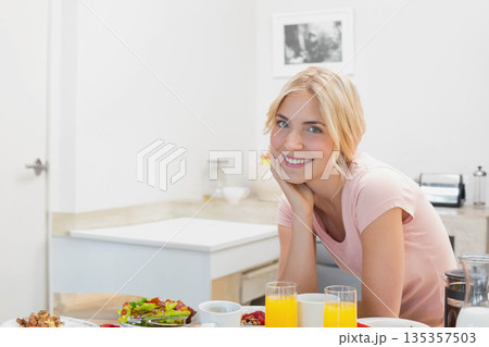 Woman leaning on kitchen countertop with orange juice fruit and cereal bowls, copy space Woman leaning on kitchen countertop with orange juice fruit and cereal bowls, copy space 135357503
