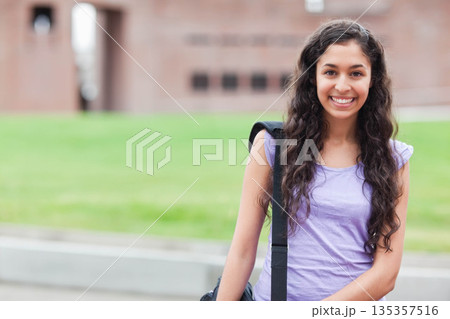 Hispanic student standing on campus path right side holding black bag strap and smiling, copy space 135357516