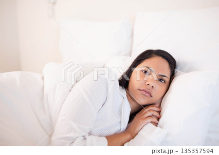 Woman lying on bed wearing white pajama top in bedroom with pillows and duvet, copy space Woman lying on bed wearing white pajama top in bedroom with pillows and duvet, copy space 135357594