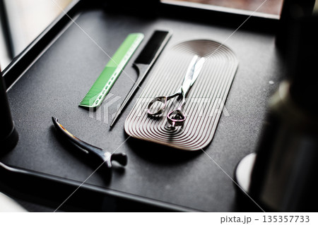 Hairdresser tools, including green comb and scissors, laid out on black tray. Hair styling accessories for professional salon service Hairdresser tools, including green comb and scissors, laid out on black tray. Hair styling accessories for professional salon service 135357733