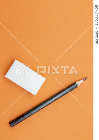 オレンジ背景に置かれた鉛筆と消しゴム 135357769