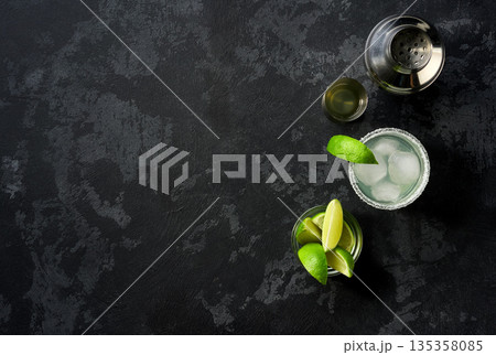 Margarita cocktail with ice cubes in glass and lime on a black table , top view. Margarita cocktail with ice cubes in glass and lime on a black table , top view. 135358085