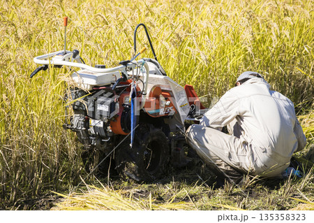 稲刈りイメージ　手押しの稲刈り機バインダーの不具合を調整する男性 135358323