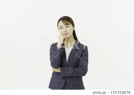 白背景の顎に手を当てて悩むスーツを着た日本人の若い女性 135358676