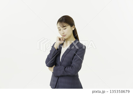 白背景の顎に手を当てて悩むスーツを着た日本人の若い女性 135358679