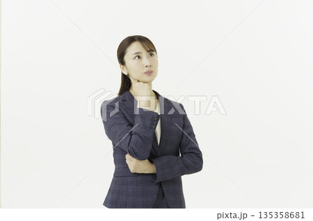 白背景の顎に手を当てて悩むスーツを着た日本人の若い女性 135358681