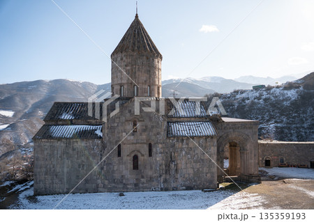 Stone church of the Tatev monastery stands against snowy mountains under clear winter sky, gray masonry, sharp light, calm and timeless mood 135359193