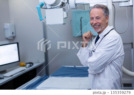 Senior male doctor standing by X-ray machine in radiology room wearing lab coat, stethoscope 135359279